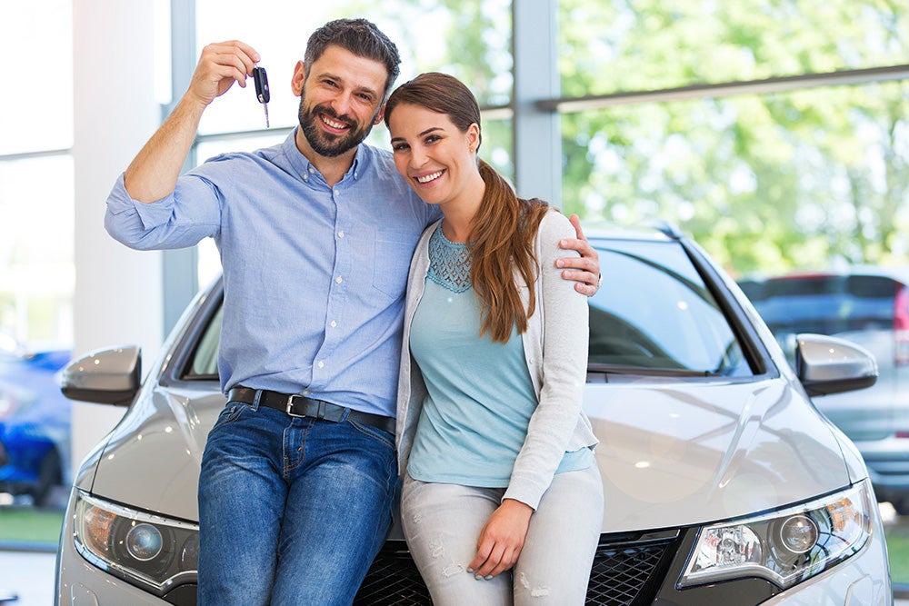 Couple holding the keys to their new car in the showroom